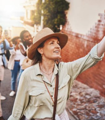 Travel, education and a teacher with students on school field trip, on urban tour. Woman, city guide and group of happy tourists, pointing at local architecture and learning on international holiday.